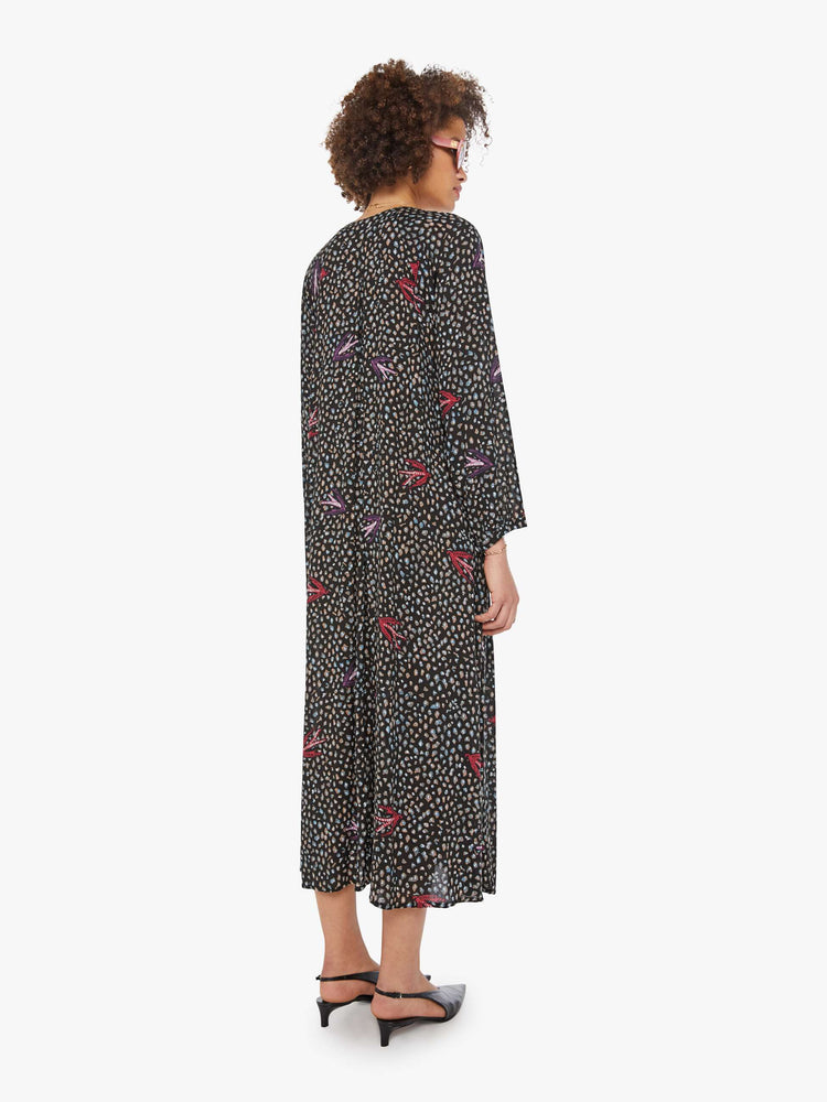 Back view of a woman in a black with white polka dots and red swallows throughout, this maxi dress has an A-line cut for a loose, breezy feel.