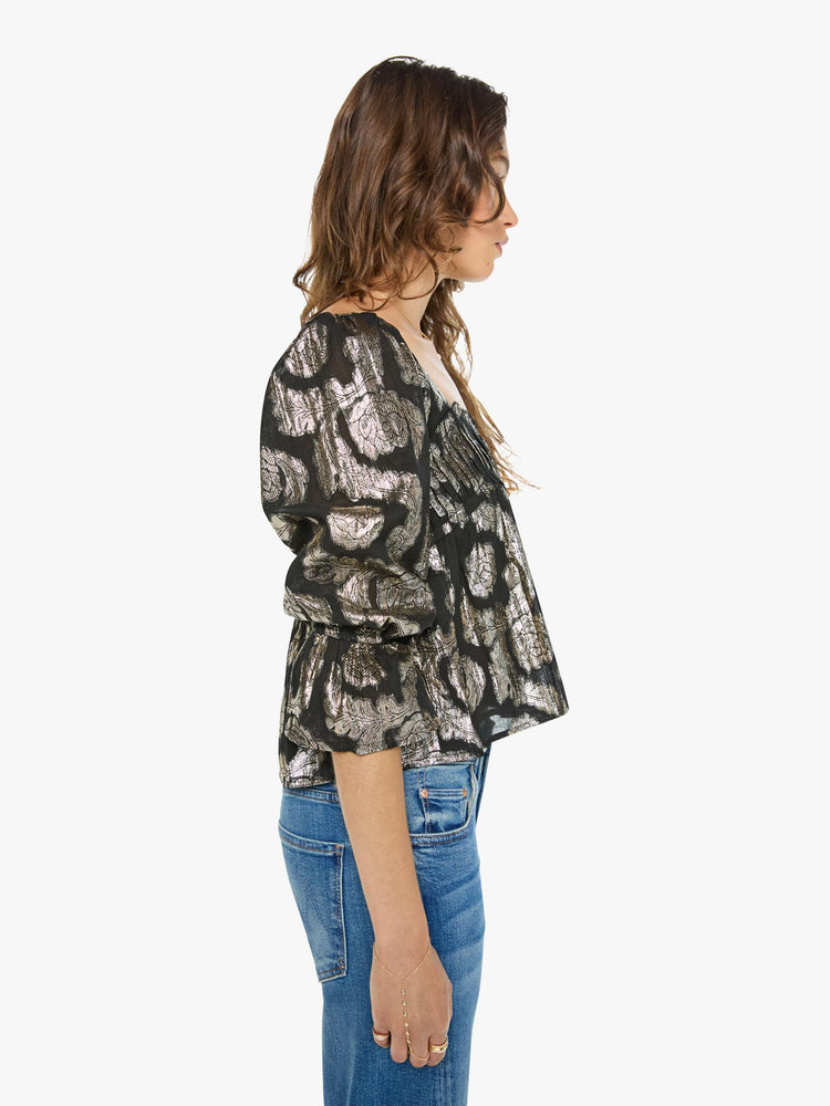 Side view of woman top in black with a metallic graphic print, and features a square neck, elbow-length balloon sleeves with a wide ruffled hem and a cropped, flowy fit.
