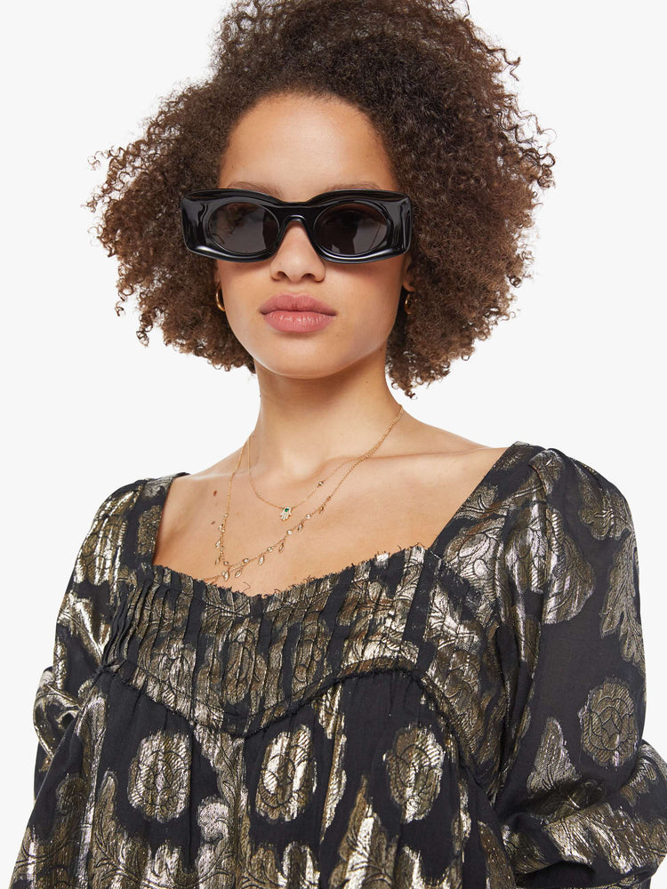 Close up view of woman top in black with a metallic graphic print, and features a square neck, elbow-length balloon sleeves with a wide ruffled hem and a cropped, flowy fit.