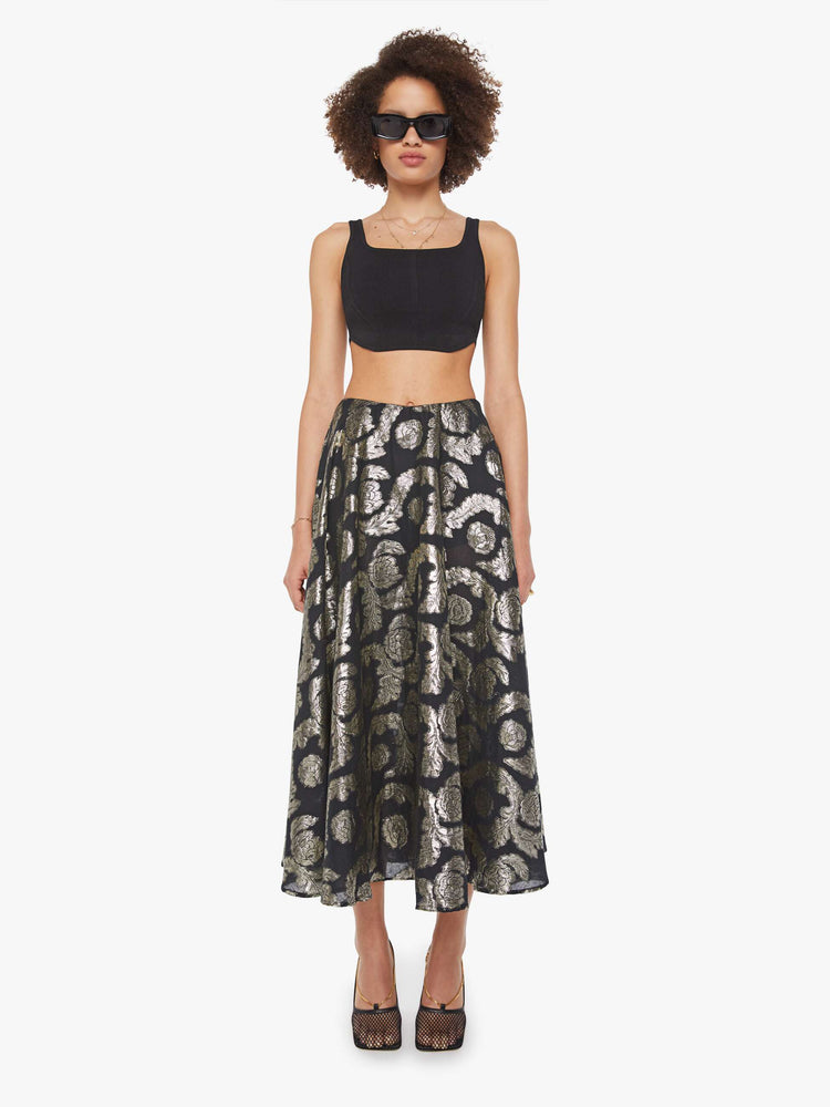 Front view of a woman in a black skirt with a metallic graphic print, and features a high waist and a loose, flowy fit.