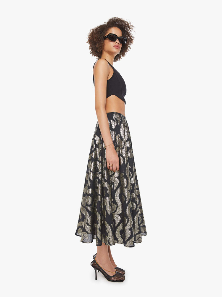 Side view of a woman in a black skirt with a metallic graphic print, and features a high waist and a loose, flowy fit.