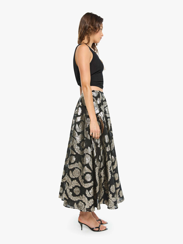 Side view of a woman in a black skirt with a metallic graphic print, and features a high waist and a loose, flowy fit.