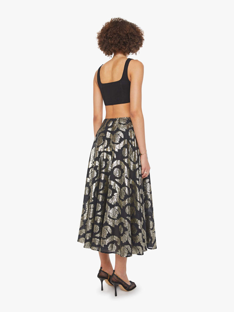 Back view of a woman in a black skirt with a metallic graphic print, and features a high waist and a loose, flowy fit.