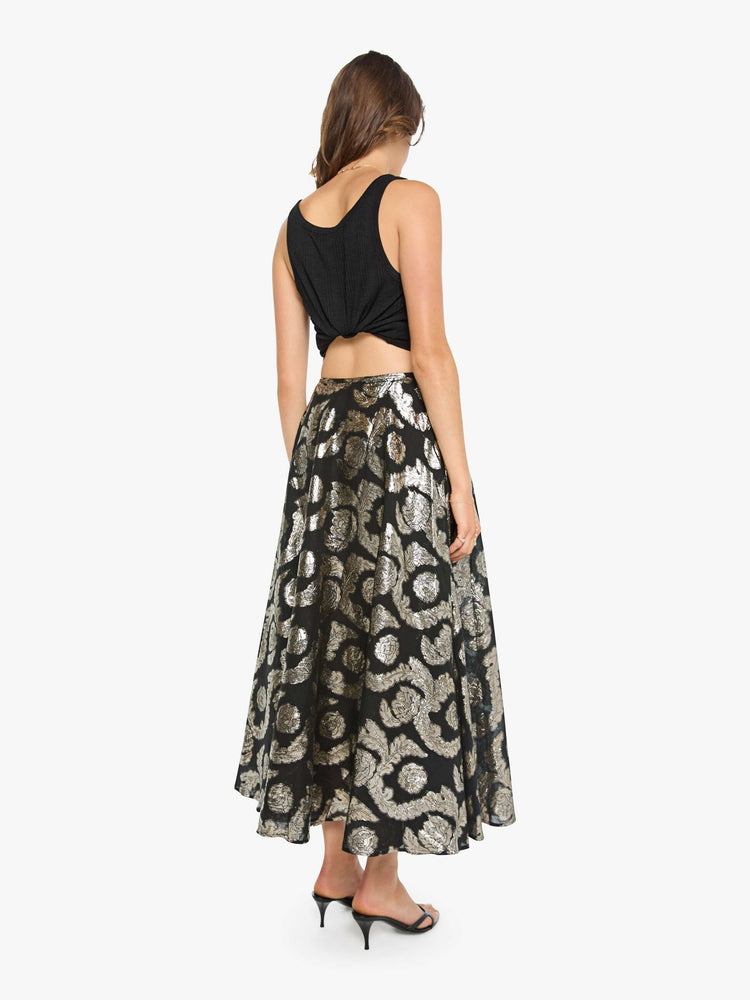 Back view of a woman in a black skirt with a metallic graphic print, and features a high waist and a loose, flowy fit.