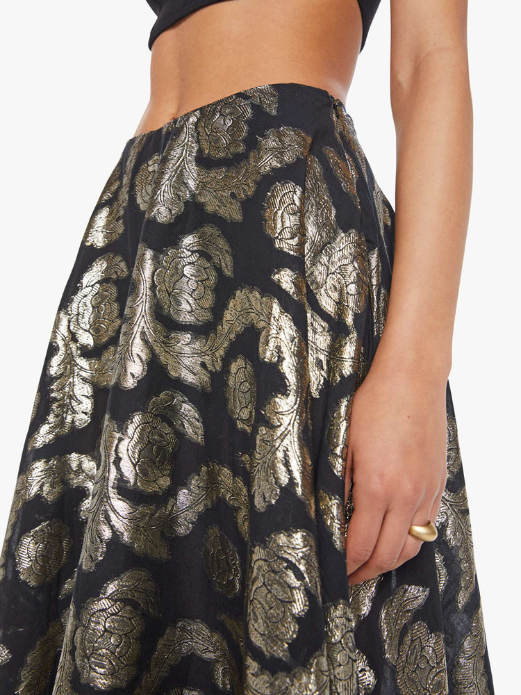 Close up view of a woman in a black skirt with a metallic graphic print, and features a high waist and a loose, flowy fit.