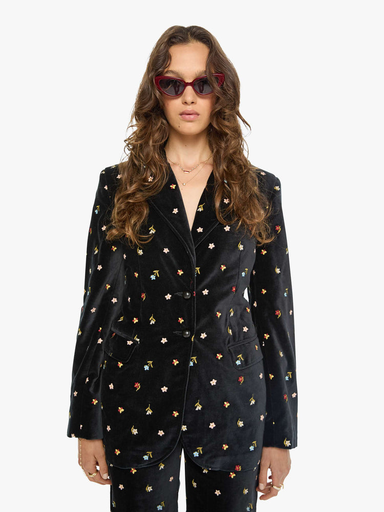 Front view of a woman in a black with colorful floral details jacket with a notched collar, padded shoulders and a classic tailored fit. 