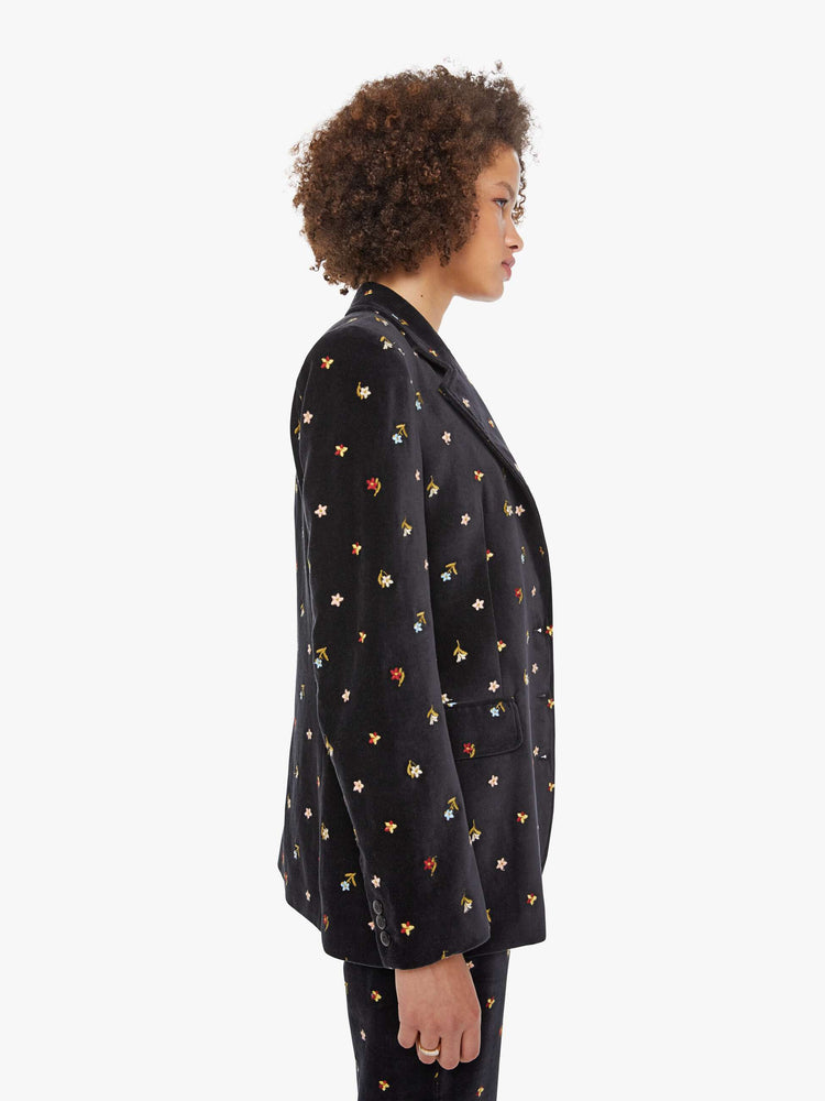 Side view of a woman in a black with colorful floral details jacket with a notched collar, padded shoulders and a classic tailored fit. 