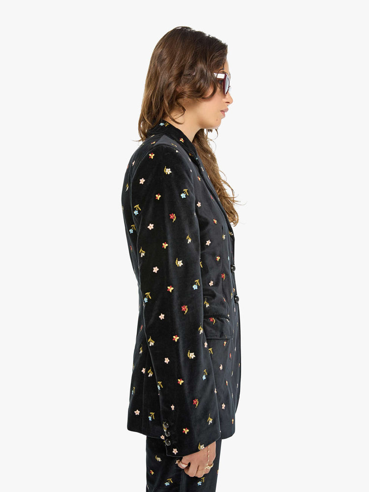 Side view of a woman in a black with colorful floral details jacket with a notched collar, padded shoulders and a classic tailored fit. 