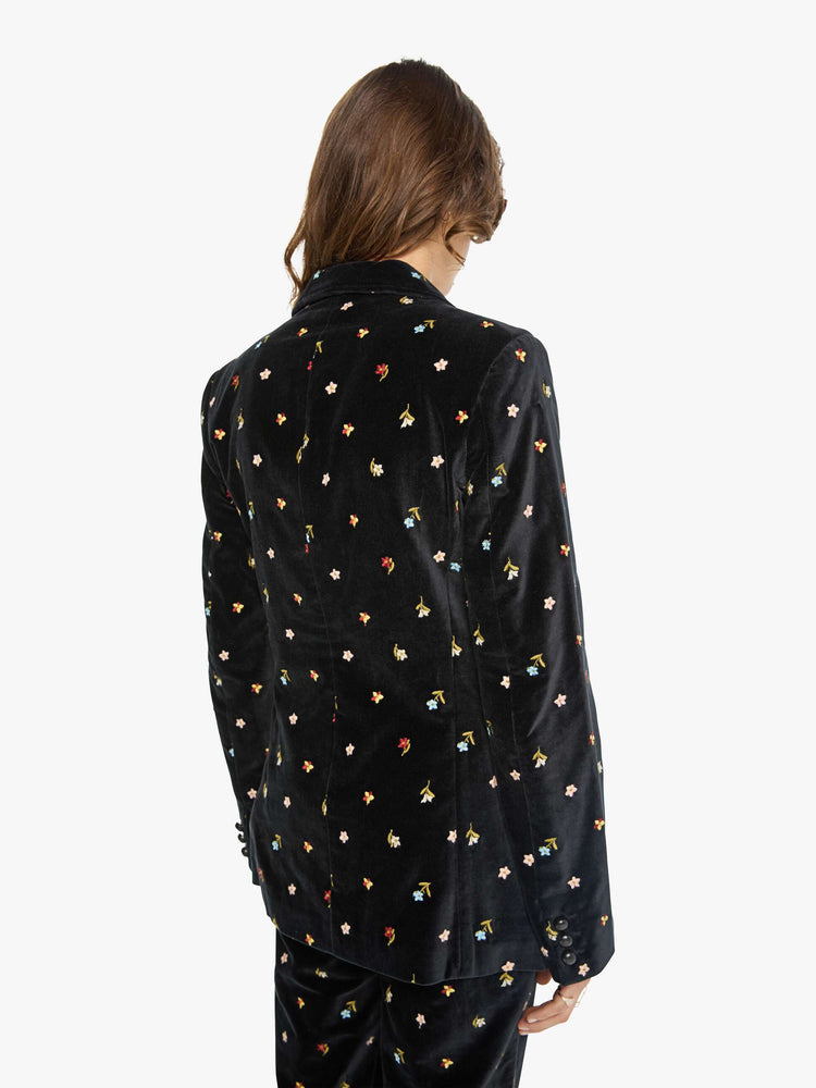 Back view of a woman in a black with colorful floral details jacket with a notched collar, padded shoulders and a classic tailored fit. 