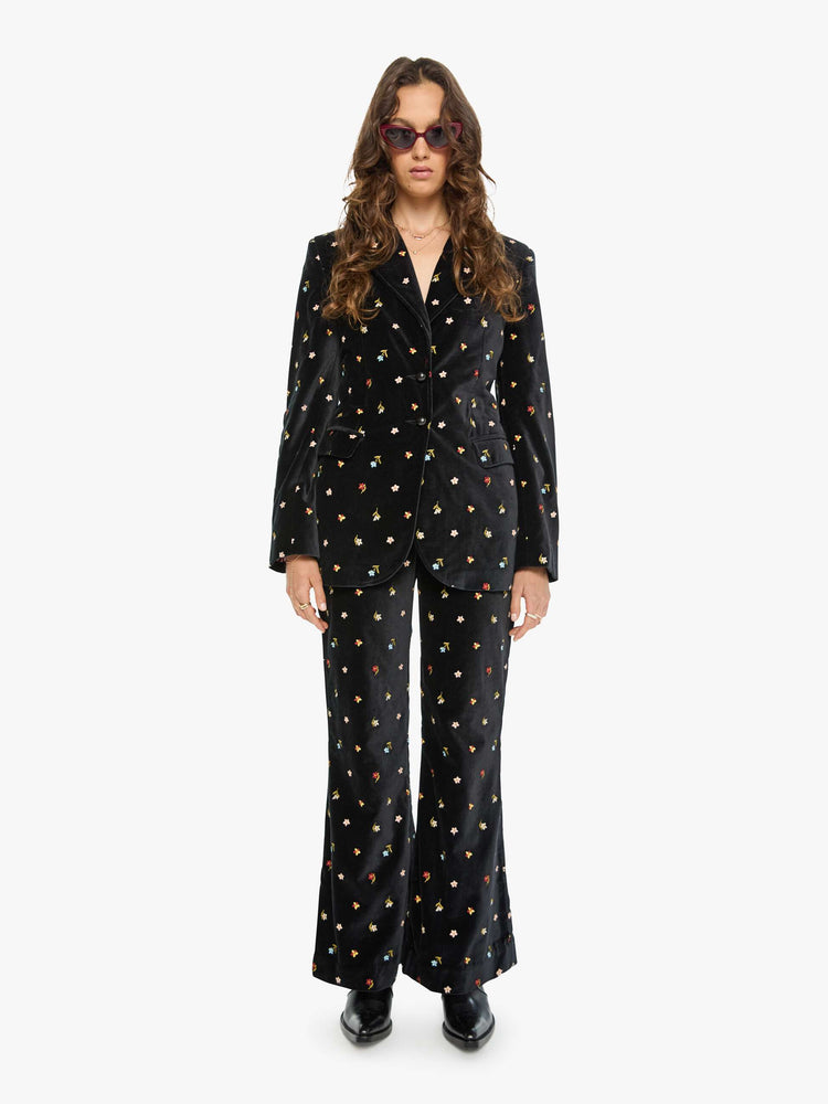 Full body view of a woman in a black with colorful floral details jacket with a notched collar, padded shoulders and a classic tailored fit.