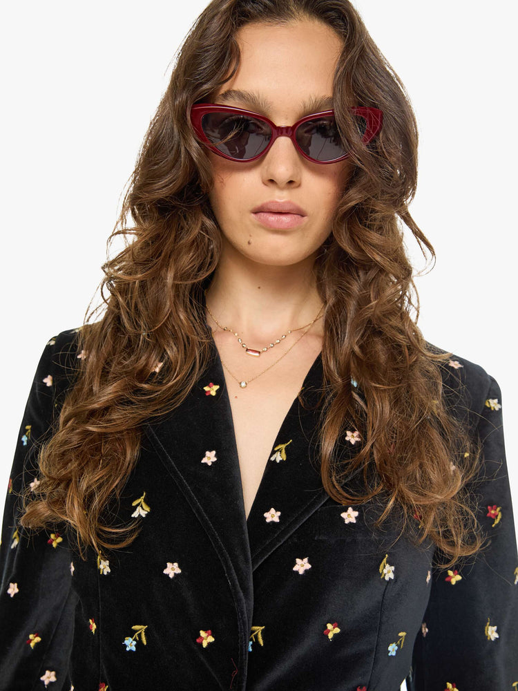 Close up view of a woman in a black with colorful floral details jacket with a notched collar, padded shoulders and a classic tailored fit. 