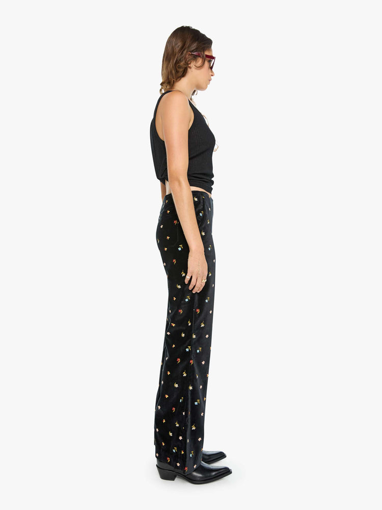 Side view of a woman in black with colorful floral details pants with a mid rise and a wide flared leg.