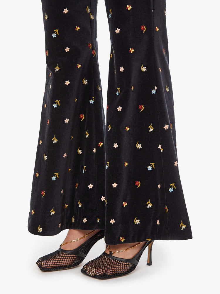 Close up view of a woman in black with colorful floral details pants with a mid rise and a wide flared leg.