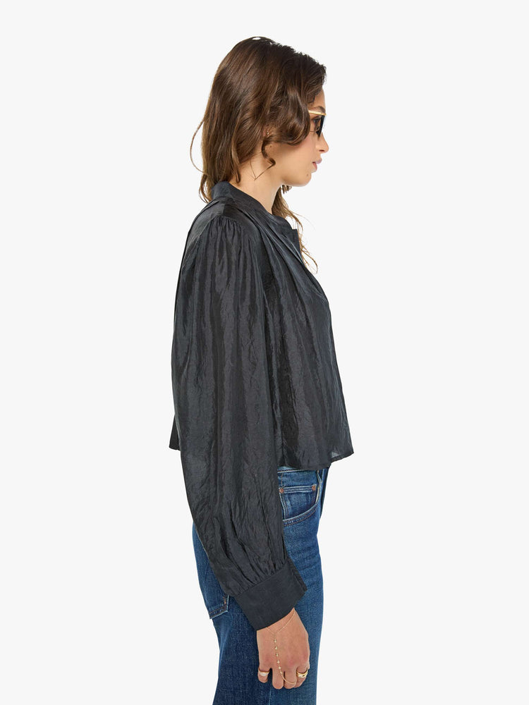 Side view of a woman in a black shirt with a collared V-neck, long balloon sleeves and a cropped fit.