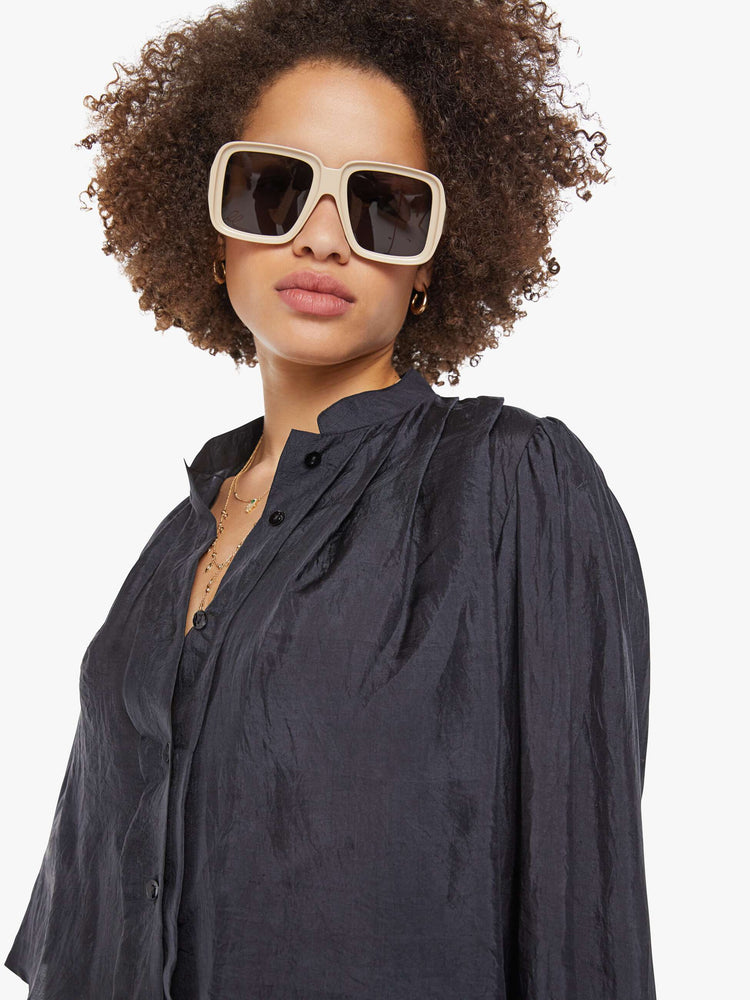 Close up view of a woman in a black shirt with a collared V-neck, long balloon sleeves and a cropped fit.