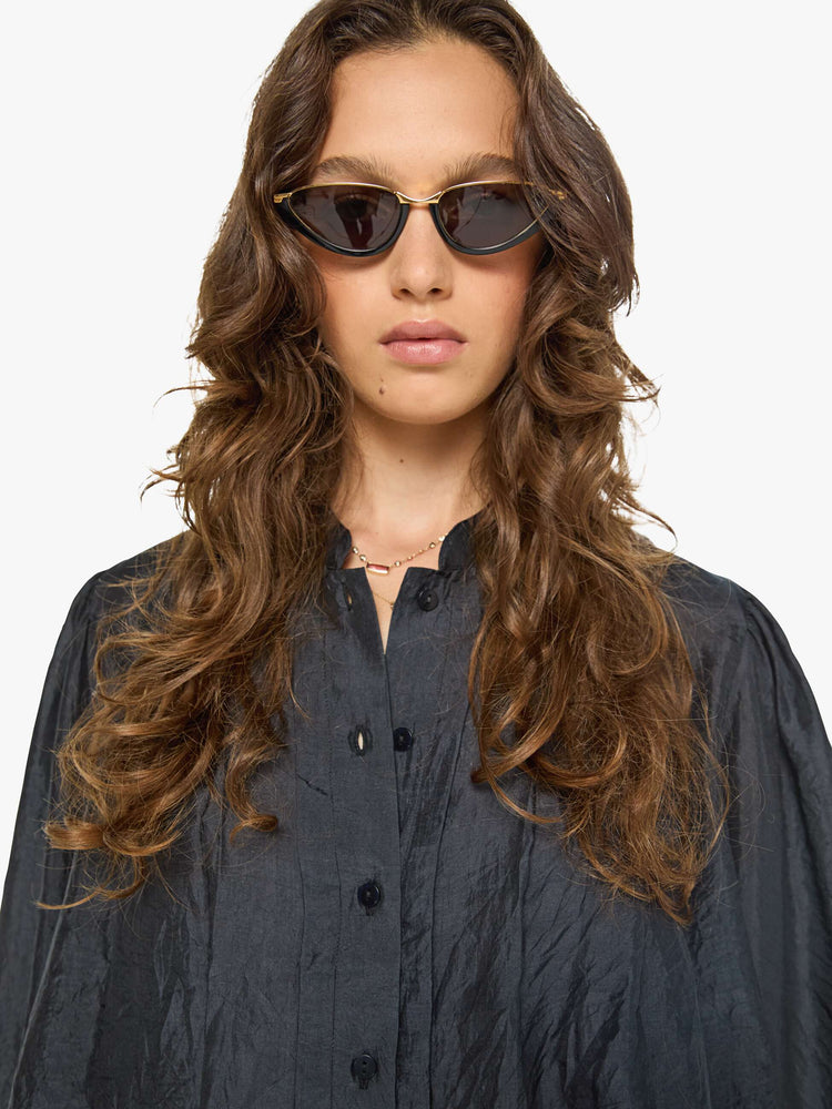 Close up view of a woman in a black shirt with a collared V-neck, long balloon sleeves and a cropped fit.