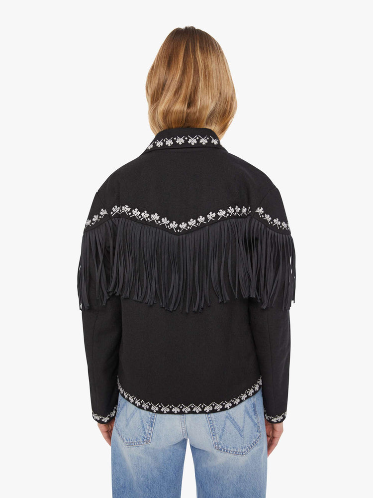 Back view of a woman in a Jacket in a black with fringe details and white embroidery with dropped shoulders, front patch pockets, buttons down the front and a boxy fit.