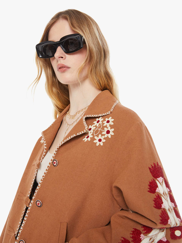 Close up view of a woman in a  Western jacket in camel with embroidered motifs throughout. It has a notched collar, buttons down the front and a boxy fit.