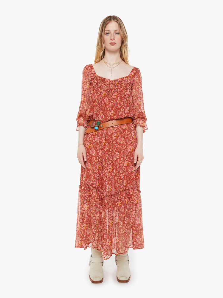 Styling view of a woman in a burnt orange with a warm-toned floral print dress with a square neck, 3/4-length sleeves, ruffled details and a loose, flowy fit.