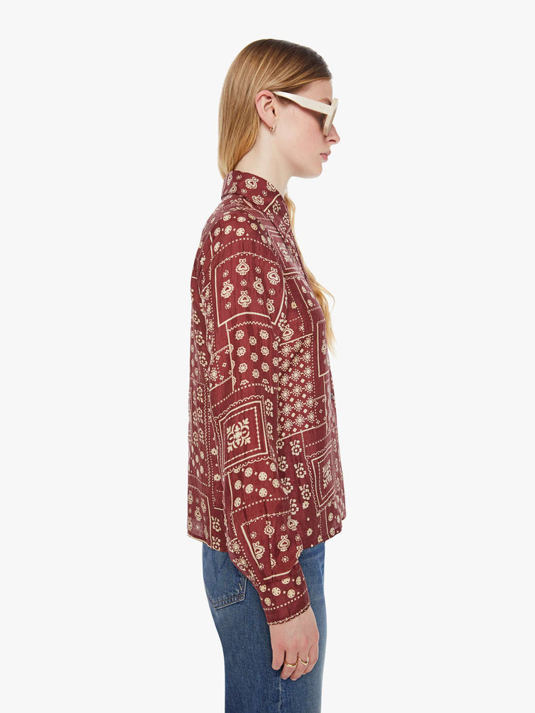 Side  view of a woman in a brown with a cream paisley print shirt with a collared neck, long sleeves and buttons down the front.