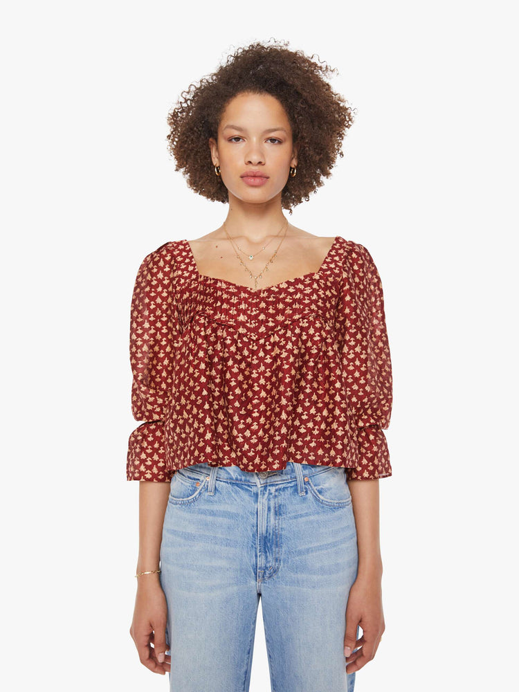 Front view of a woman in a  red with cream dots with a square neck, babydoll bodice, elbow-length balloon sleeves with a wide ruffled hem and a cropped, flowy fit.