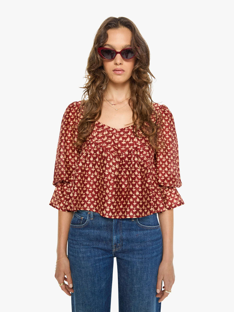 Front view of a woman in a  red with cream dots with a square neck, babydoll bodice, elbow-length balloon sleeves with a wide ruffled hem and a cropped, flowy fit.