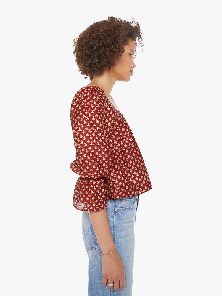 Side view of a woman in a  red with cream dots with a square neck, babydoll bodice, elbow-length balloon sleeves with a wide ruffled hem and a cropped, flowy fit.