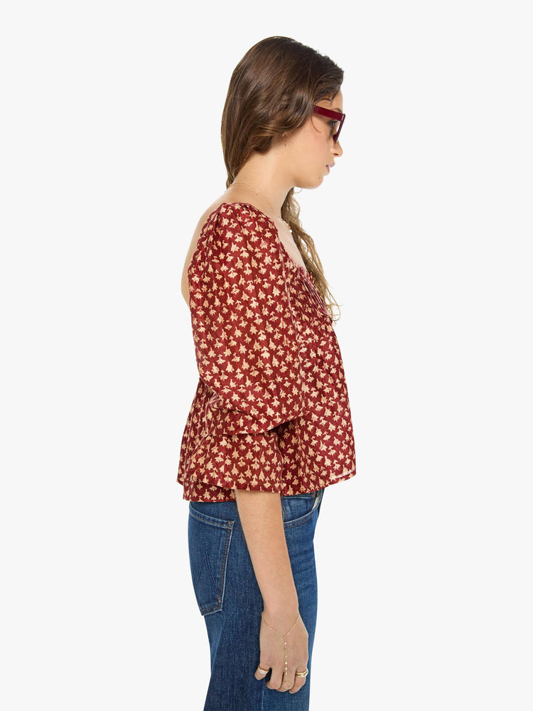 Side view of a woman in a  red with cream dots with a square neck, babydoll bodice, elbow-length balloon sleeves with a wide ruffled hem and a cropped, flowy fit.
