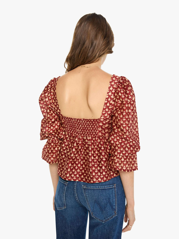 Back view of a woman in a  red with cream dots with a square neck, babydoll bodice, elbow-length balloon sleeves with a wide ruffled hem and a cropped, flowy fit.
