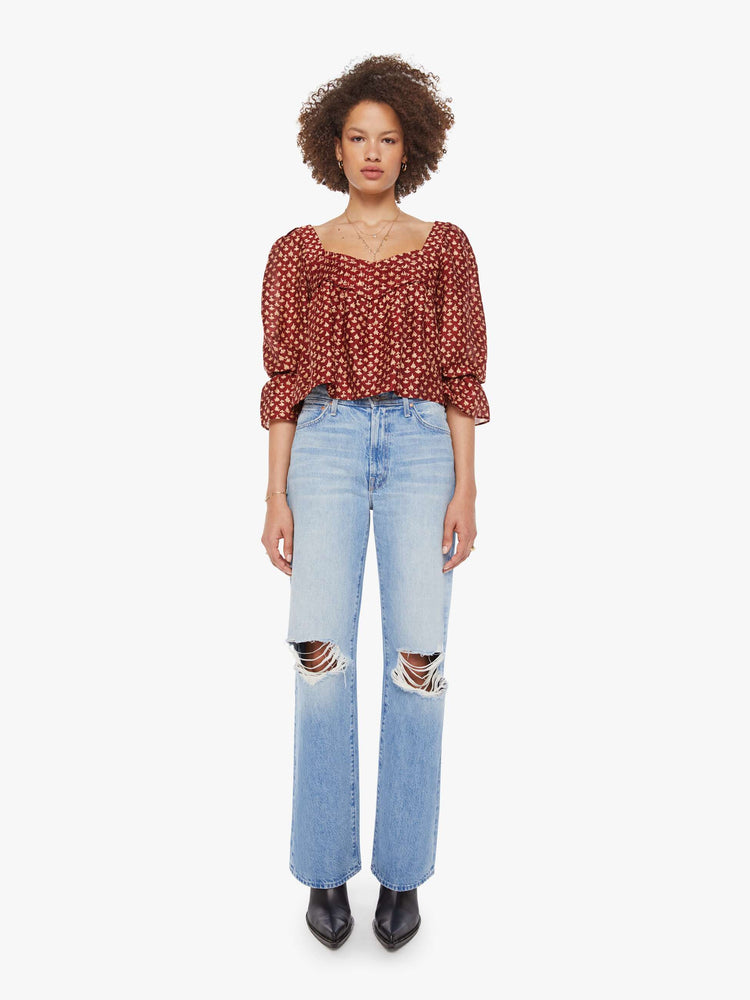 Full body view of a woman in a  red with cream dots with a square neck, babydoll bodice, elbow-length balloon sleeves with a wide ruffled hem and a cropped, flowy fit.