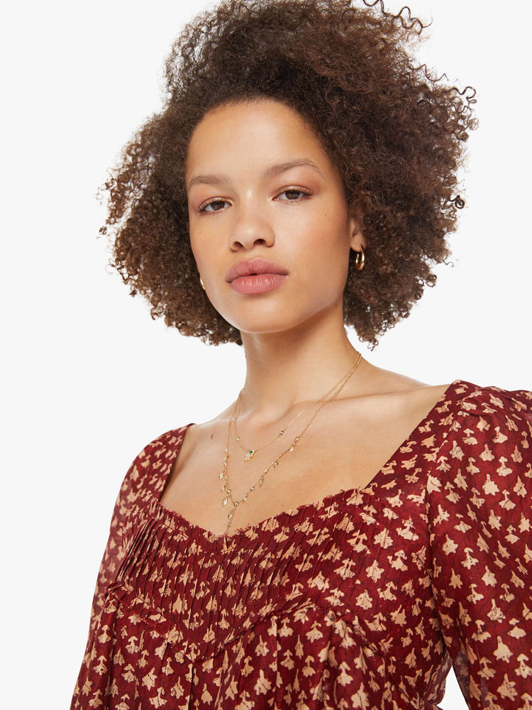 Close up view of a woman in a  red with cream dots with a square neck, babydoll bodice, elbow-length balloon sleeves with a wide ruffled hem and a cropped, flowy fit.