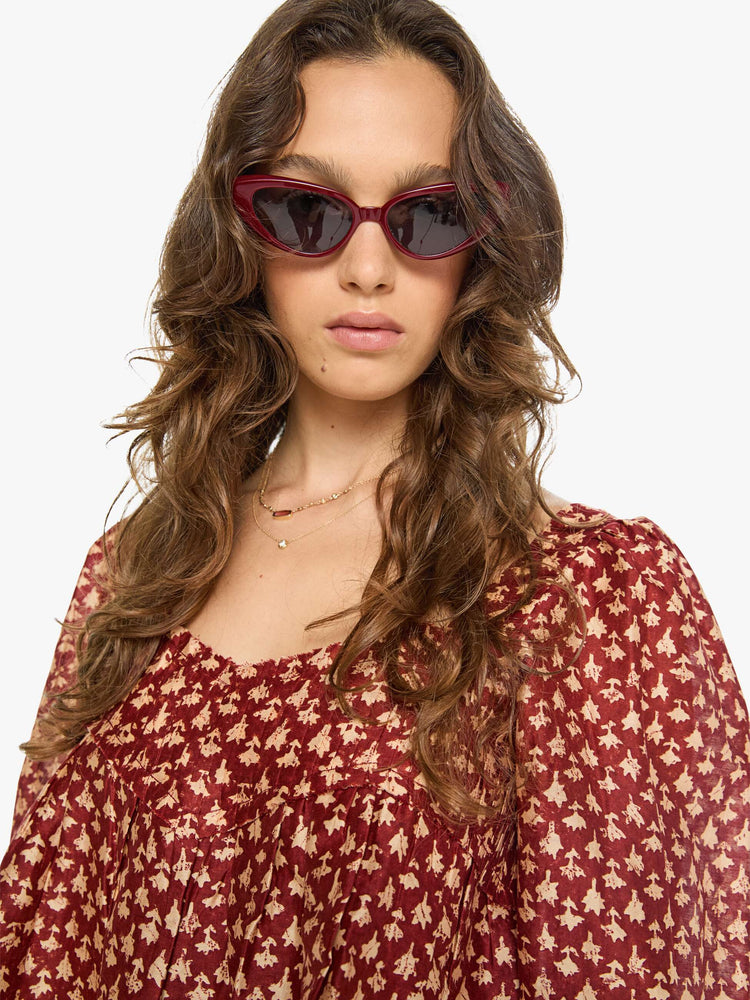 Close up view of a woman in a  red with cream dots with a square neck, babydoll bodice, elbow-length balloon sleeves with a wide ruffled hem and a cropped, flowy fit.