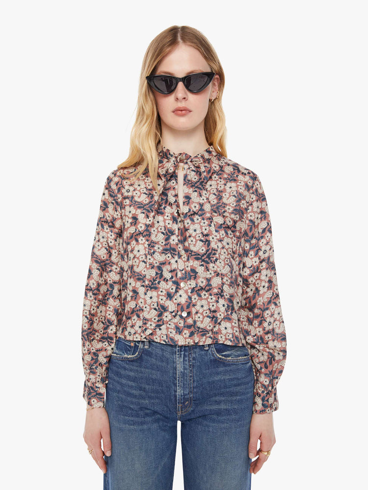 Front view of a woman pink, black and white floral print shirt with  V-neck that ties, long balloon sleeves and a slightly cropped fit.