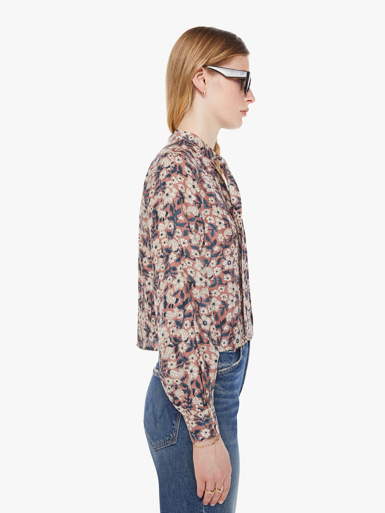 Side view of a woman pink, black and white floral print shirt with  V-neck that ties, long balloon sleeves and a slightly cropped fit.