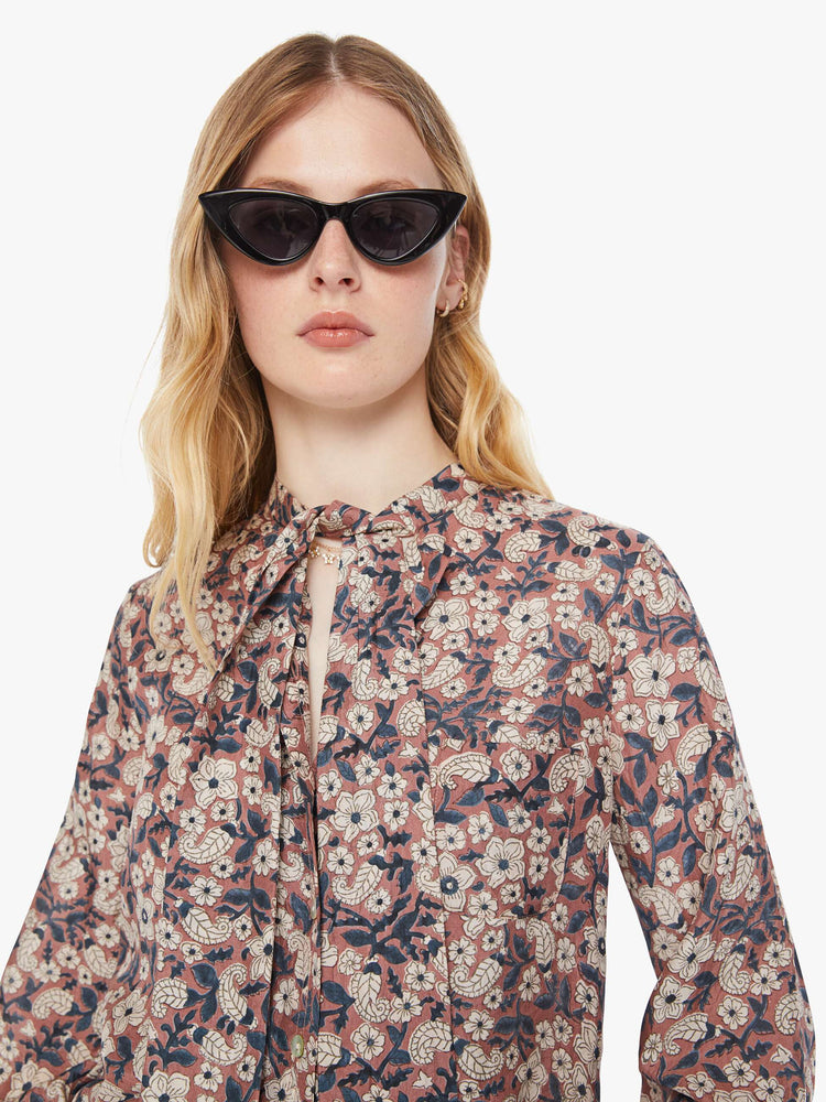 Close up view of a woman pink, black and white floral print shirt with  V-neck that ties, long balloon sleeves and a slightly cropped fit.