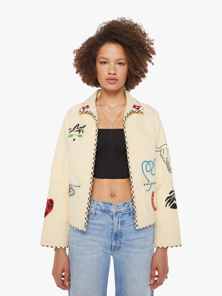 Front view of a woman in a cream jacket with beaded motifs and slightly dropped shoulders, front patch pockets and a tailored fit that hugs the body like a blazer.