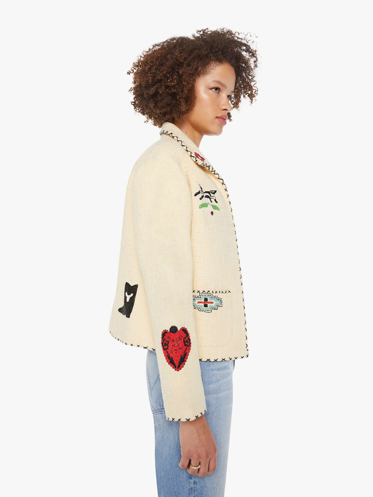 Side view of a woman in a cream jacket with beaded motifs and slightly dropped shoulders, front patch pockets and a tailored fit that hugs the body like a blazer.