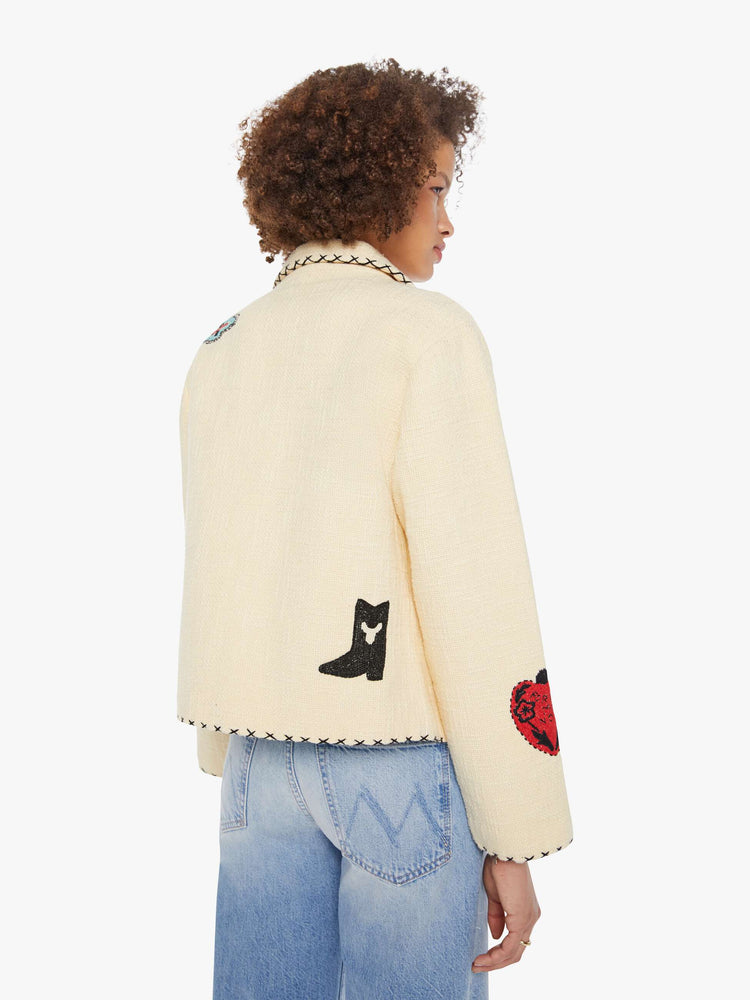 Back view of a woman in a cream jacket with beaded motifs and slightly dropped shoulders, front patch pockets and a tailored fit that hugs the body like a blazer.