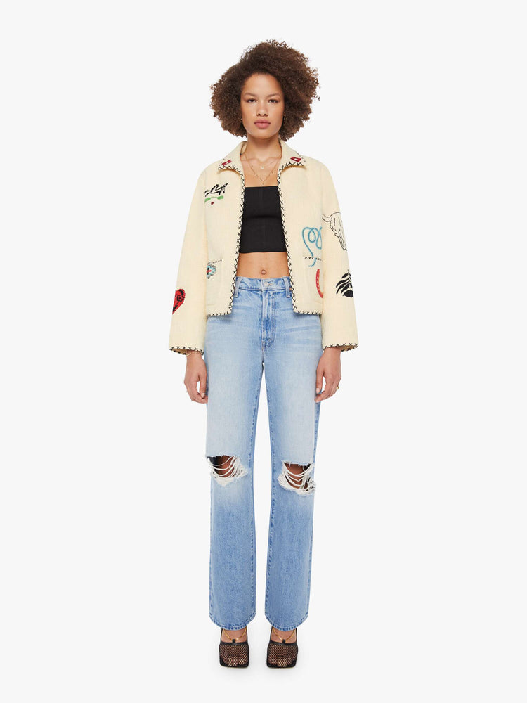 Full body view of a woman in a cream jacket with beaded motifs and slightly dropped shoulders, front patch pockets and a tailored fit that hugs the body like a blazer.