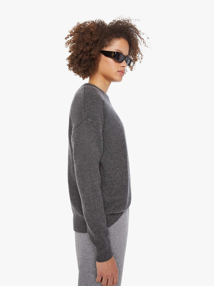 Side view of a woman in a sweater  cashmere in dark grey, the sweater has a crewneck, drop shoulders and a loose, comfortable fit.