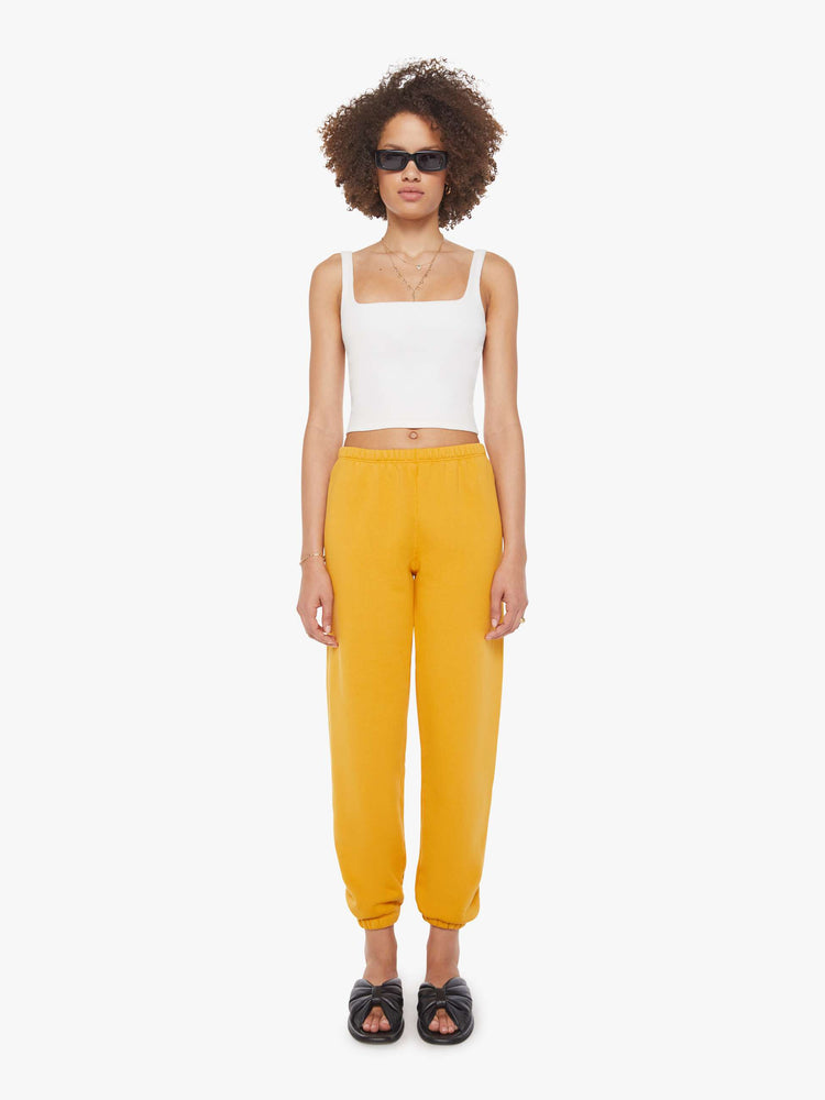 Front view of a woman in a yellow sweatpants with an elastic waist and cuffs for a loose and a white logo on the ankle.