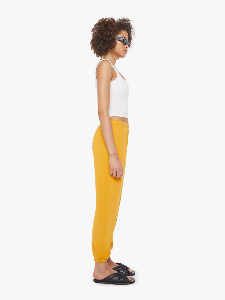 Side view of a woman in a yellow sweatpants with an elastic waist and cuffs for a loose and a white logo on the ankle.