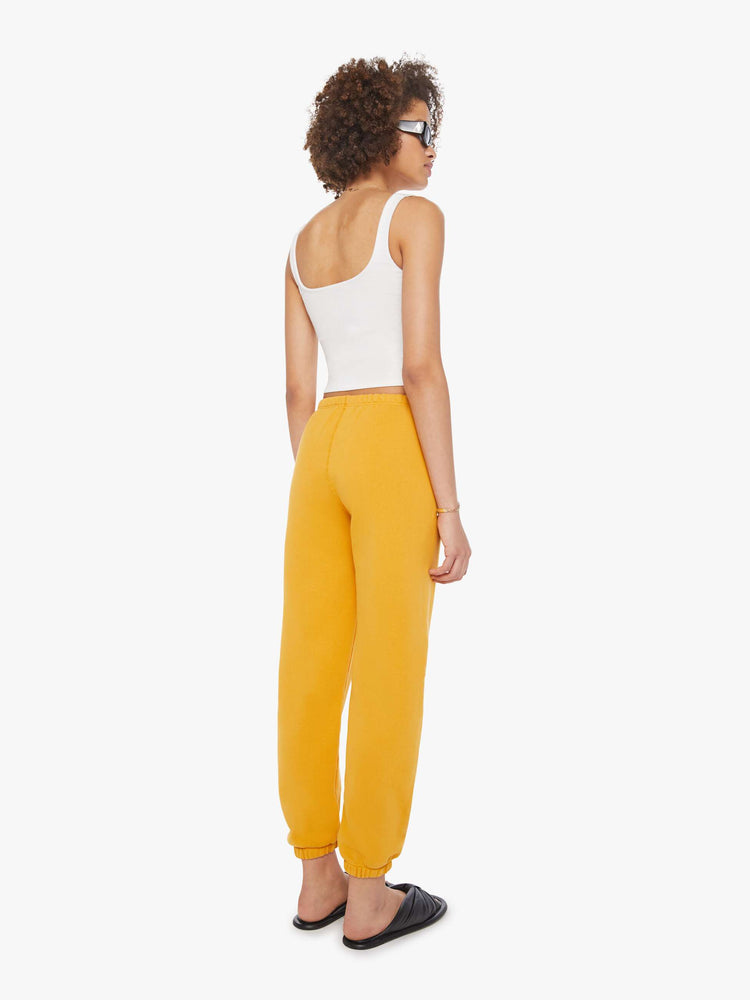 Back view of a woman in a yellow sweatpants with an elastic waist and cuffs for a loose and a white logo on the ankle.