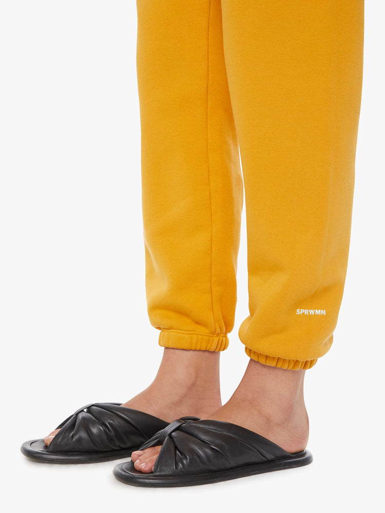 Close up view of a woman in a yellow sweatpants with an elastic waist and cuffs for a loose and a white logo on the ankle.