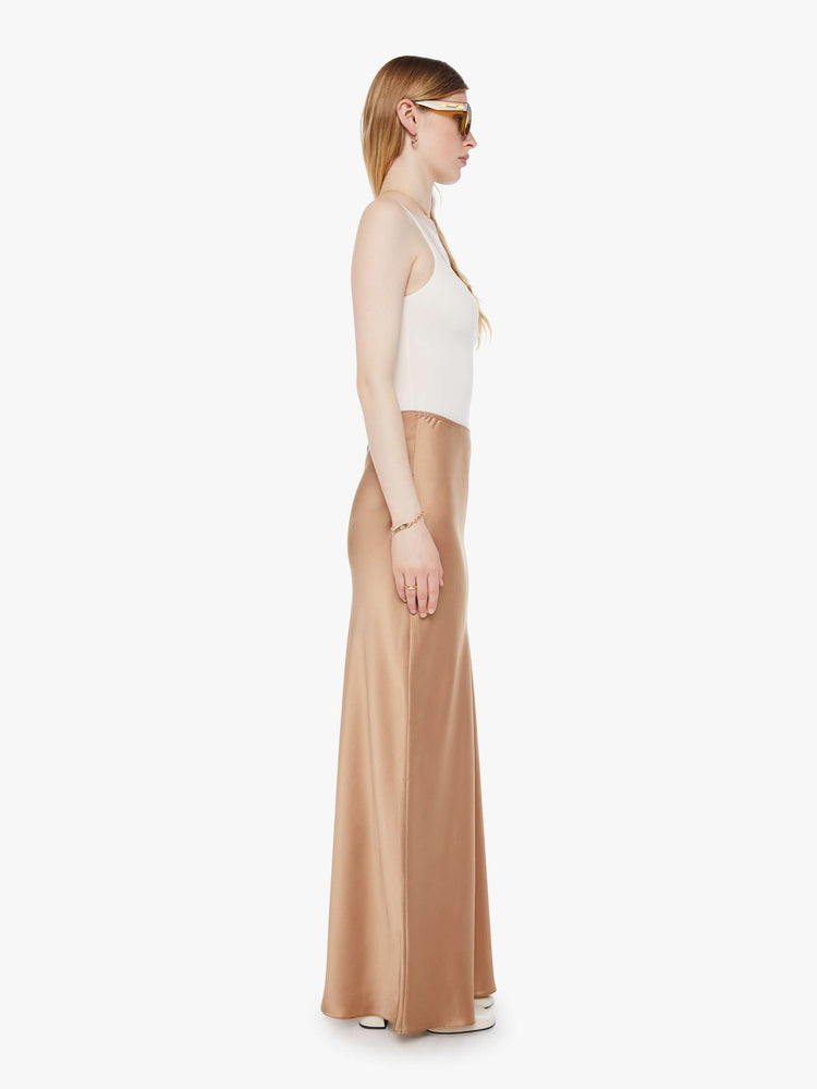 Side view of a woman in a light khaki bias cut maxi skirt with a straight fit and a flowy ankle-grazing hem.