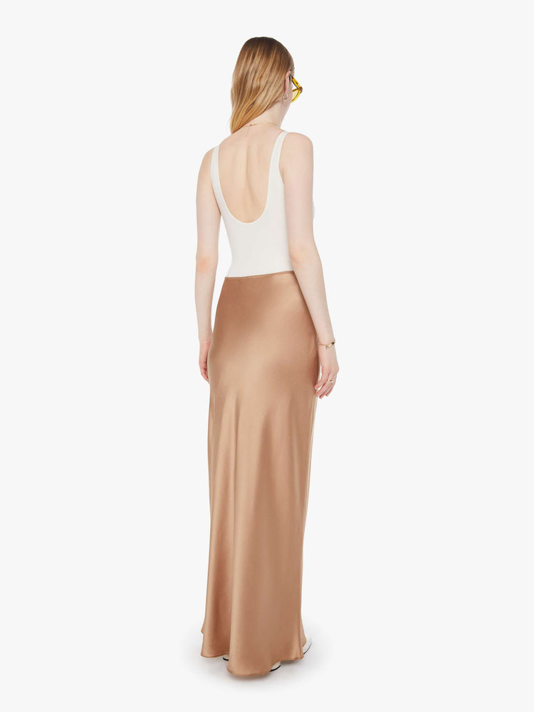 Back view of a woman in a light khaki bias cut maxi skirt with a straight fit and a flowy ankle-grazing hem.