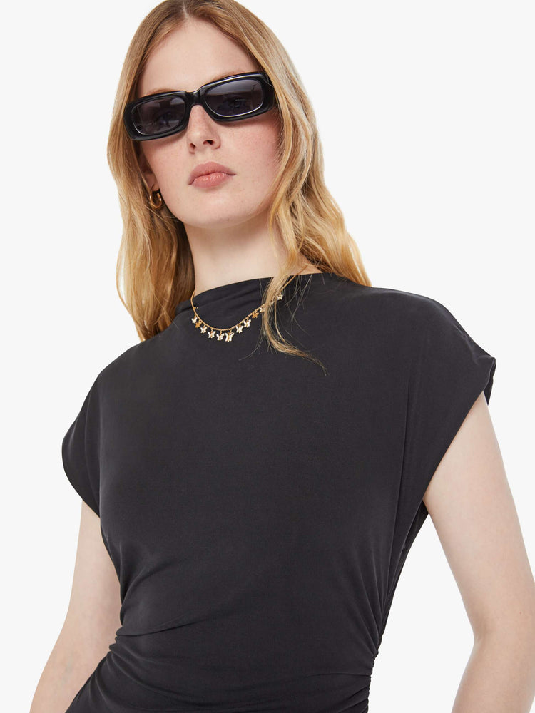 Close up view of a woman in a black midi dress designed with a mock neck, short sleeves, a narrow fit and calf-grazing hem.