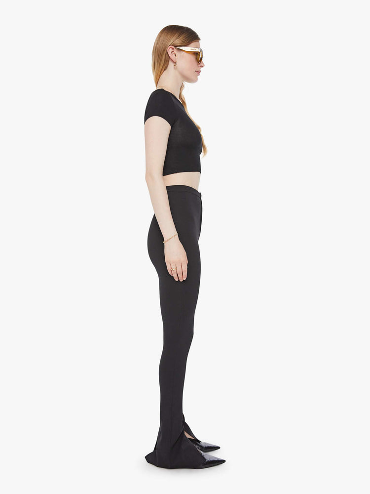 Side view of a woman in a black high rise pant and an extra-long inseam with a split hem.