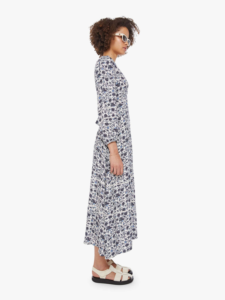 Side view of a woman in a white and navy floral print dress with a V-neck, 3/4-length sleeves and a loose, flowy fit.