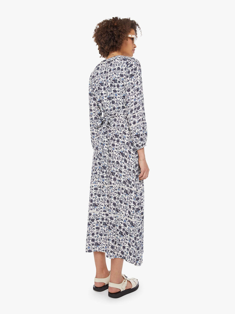 Back view of a woman in a white and navy floral print dress with a V-neck, 3/4-length sleeves and a loose, flowy fit.